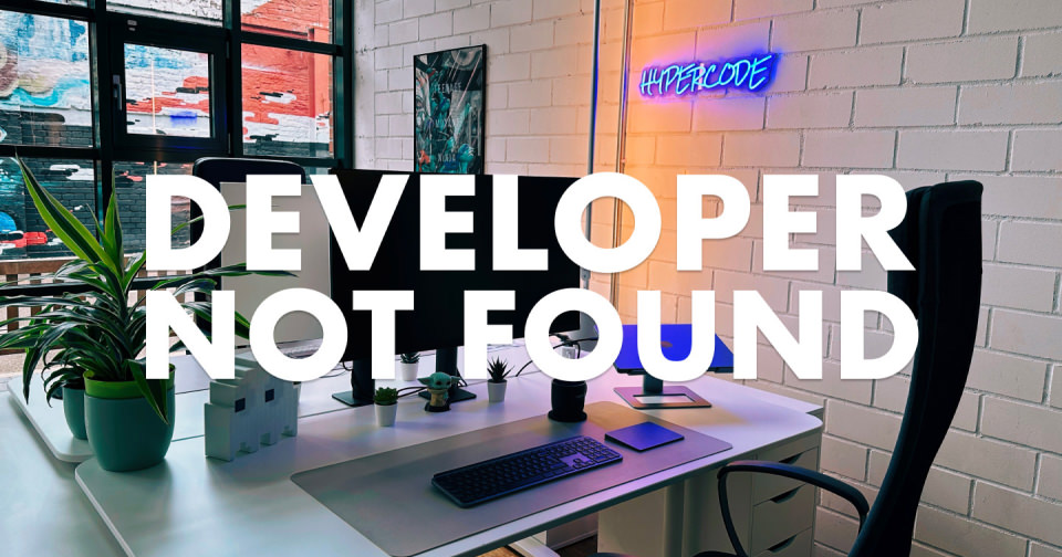 Moderner Arbeitsplatz im Hypercode-Büro in Pulheim bei Köln mit großem Schreibtisch, zwei Monitoren, Pflanzen und ergonomischem Stuhl vor einer hellen Backsteinwand; im Hintergrund leuchtet ein blaues Neon-„HYPERCODE“-Logo, darüber liegt der Schriftzug „Developer not found“.